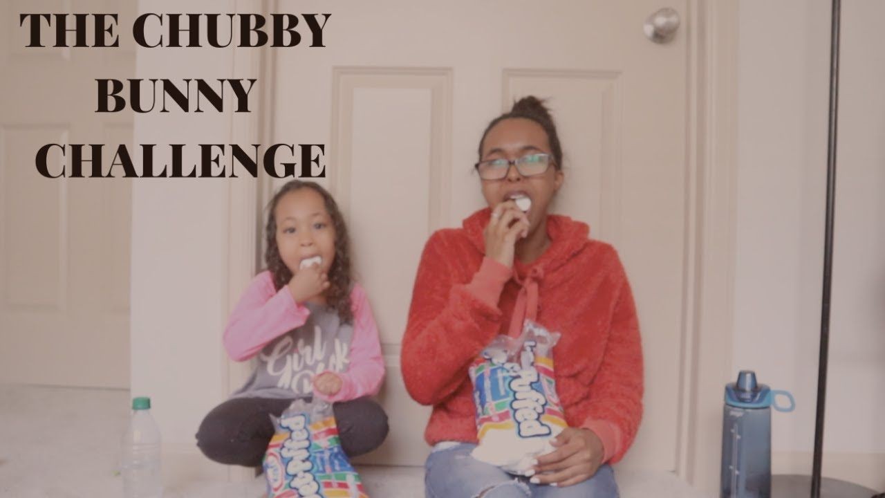 Two people sitting on the floor doing the Chubby Bunny Challenge with marshmallows.