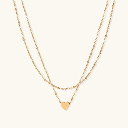 Delicate double-chain gold necklace with tiny heart pendant on cream background